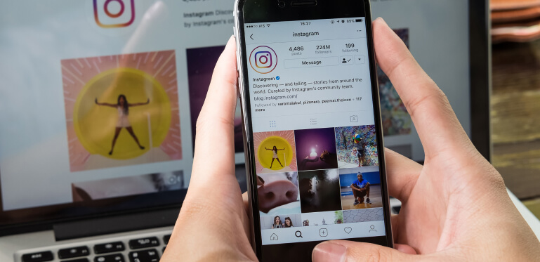 Um par de mãos segurando um celular emf rente ao computador com o instagram aberto em ambos os dispositivos