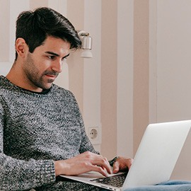 a imagem mostra um homem sentado com um notebook no colo. Ele está navegando na internet, provavelmente ele compra em lojas virtuais de roupas masculinas.