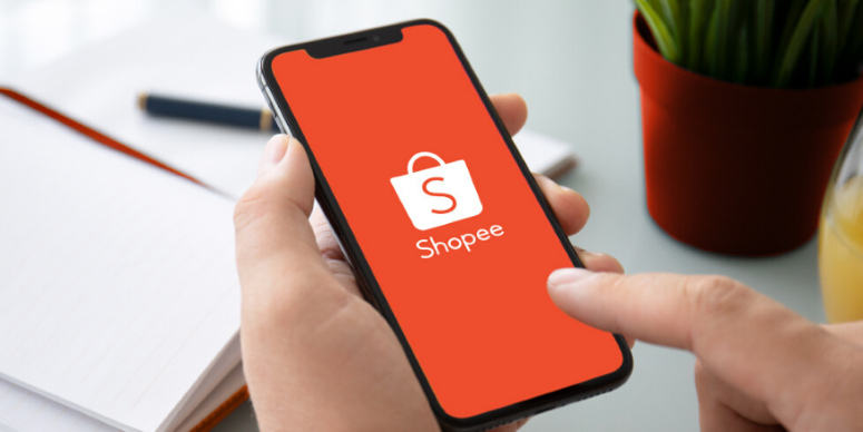 a imagem mostra uma mão segurando um celular conectado à tela inicial do App da Shopee