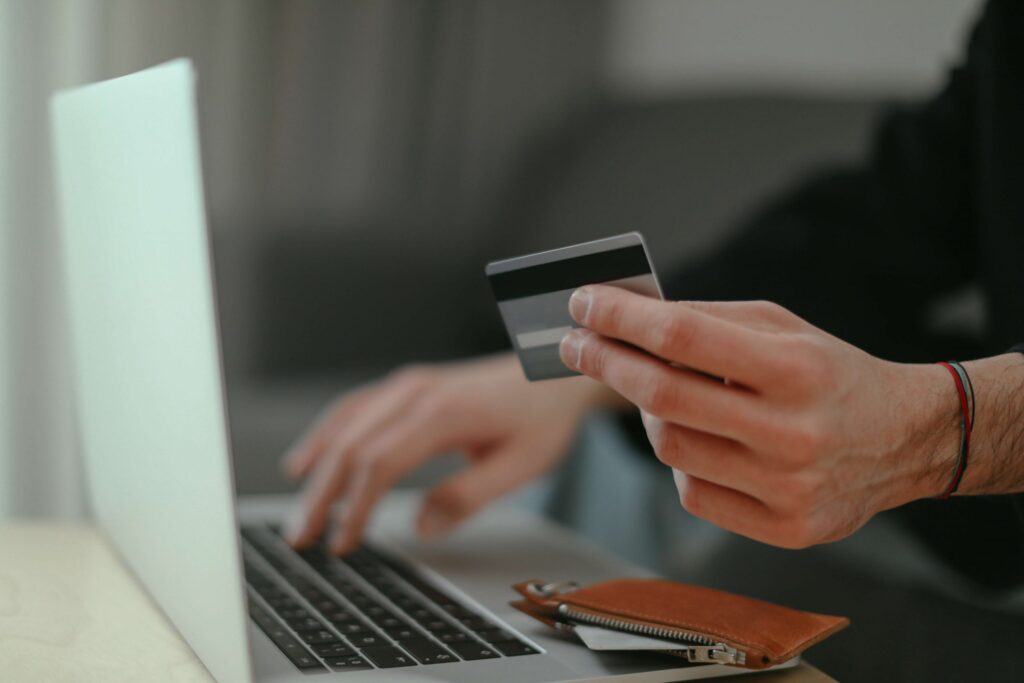 a imagem mostra uma pessoa segurando um cartão de crédito, na frente de um computador, provavelmente ela está realizando algum pagamento online.