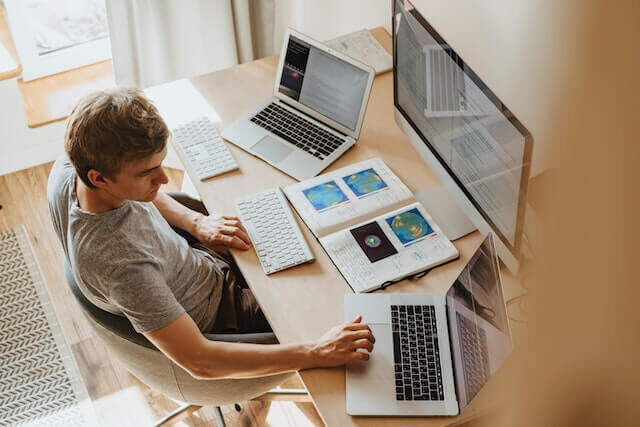 a imagem mostra um homem em sua estação de trabalho. Ele está trabalhando com 3 telas, um computador e dois notebooks. Provavelmente ele faz uso de plataformas digitais para otimizar seus processos.