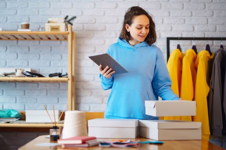 a imagem mostra uma mulher branca, embalando produtos que ela vendeu no seu e-commerce.