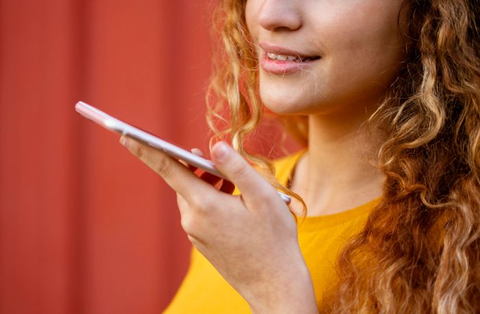 a imagem mostra em close uma garota segurando smartphone. Ela está realizando uma busca por voz. 
