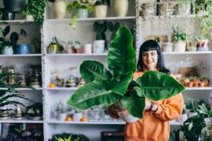 a imagem mostra uma mulher segurando uma planta decorativa ben grande e bonita. Ela está feliz pois montou sua loja virtual de decoração