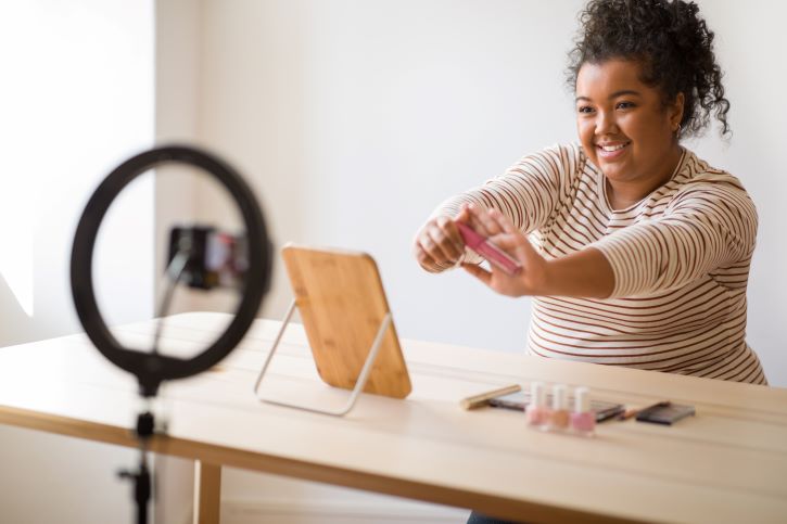 a imagem mostra uma mulher fazendo live de produtos de maquiagem. Ela é dona de uma loja virtual de maquiagens e vende pela internet.