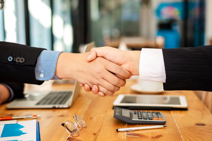 A imagem mostra dois executivos de negócios selando um contrato, apertando as mãos.