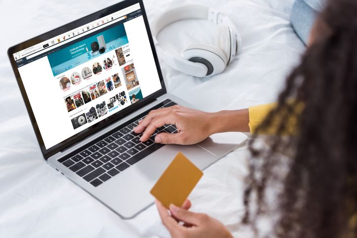 imagem recortada de mulher segurando cartão de crédito e usando laptop com a Amazon na tela