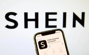 a imagem mostra um celular logado no app da Shein, e ao fundo a logo da Shein