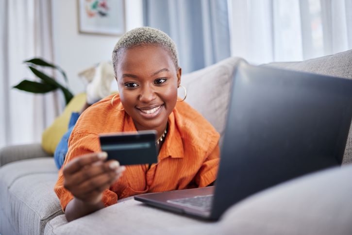 a imagem mostra uma mulhe negra no sofá fazendo uma compra online.