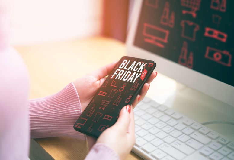 Mãos de mulher olhando no celular um banner com ofertas de Black Friday
