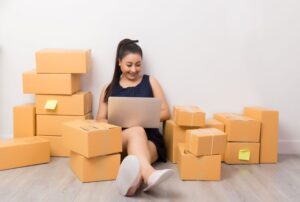 Como vender pela internet - mulher em casa rodeada de caixas vendendo produtos online