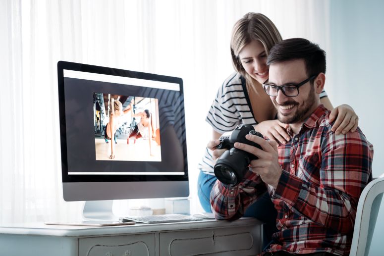 Casal analisando fotos em câmera e computador — ilustrando como vender fotos na internet com qualidade e profissionalismo.