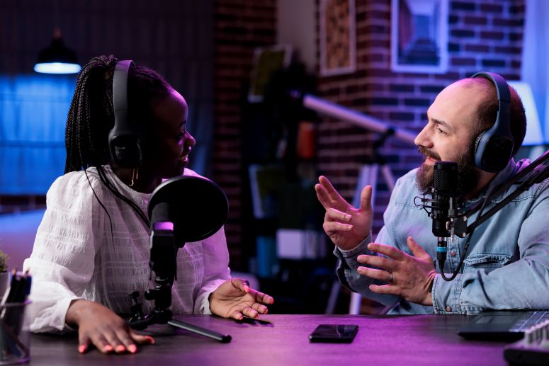Duas pessoas gravando um podcast sobre empreendedorismo em estúdio, usando fones de ouvido e microfones profissionais.