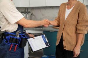Profissional autônomo apertando a mão de uma cliente em ambiente residencial, segurando uma prancheta com documentos, representando a formalização de serviços e a importância do alvará de funcionamento.