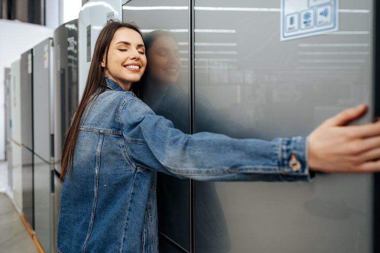 Mulher sorridente abraçando uma geladeira nova em uma loja, representando a satisfação e segurança proporcionadas pela garantia estendida na compra de eletrodomésticos.