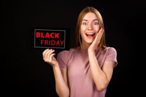A imagem mostra uma moça loira sorridente, com uma plaquinha escrita Black Friday