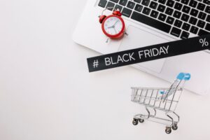 Um notebook aberto com uma placa escrito "Black Friday" e um relógio ao lado.