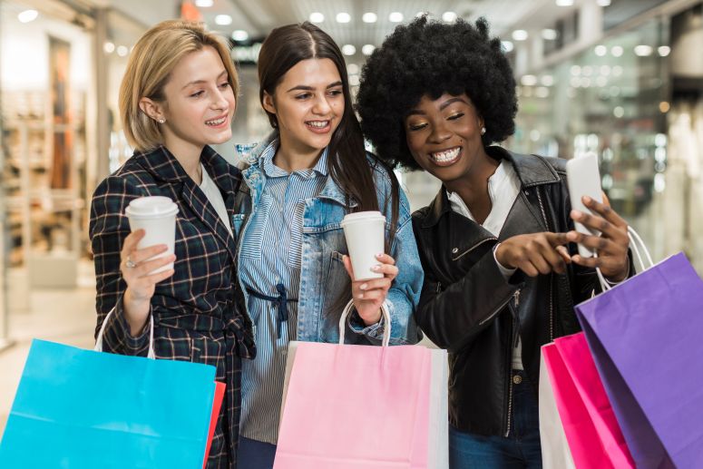 Jovens mulheres fazendo compra no shopping e olhando celular sorridentes