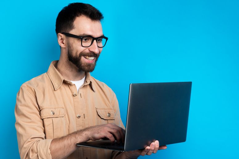 Homem em um fundo azul, usando seu notebook prateado