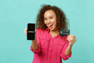 a imagem mostra uma mulher segurando um celular e um cartão de crédito. Ela está feliz pois ganhou crédito com cashback após utilizar seu cartão