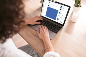 Uma mulher em frente ao notebook com a tela acessando o Facebook.