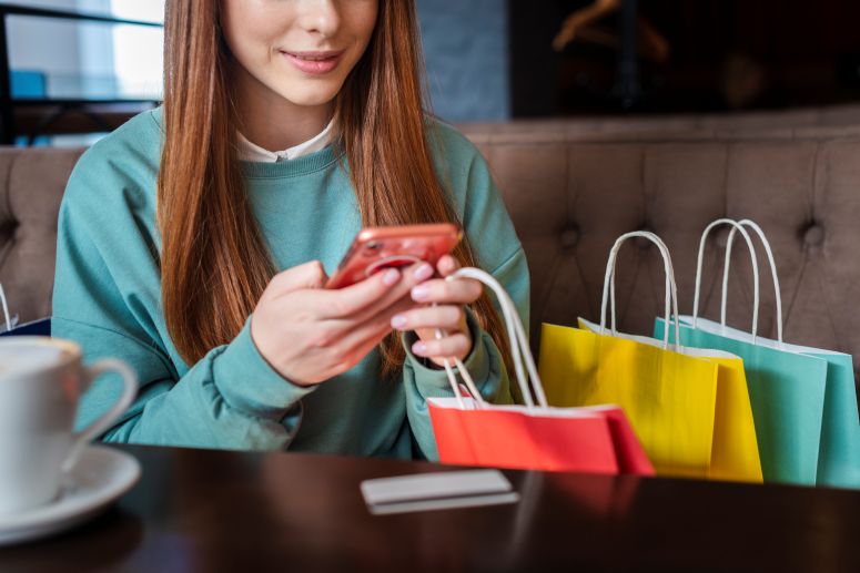 Moça cheia de sacolas de compras mexendo em seu celular