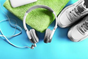 A imagem mostra alguns Itens esportivos como: toalha, fone e tênis.
