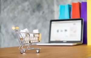 Um notebook aberto sobre uma mesa de madeira e um mini carrinho de compras.